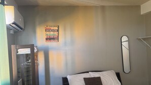 Habitación de hotel con cama, mesita de noche, espejo, aire acondicionado instalado en la pared y un cartel enmarcados con normas familiares.