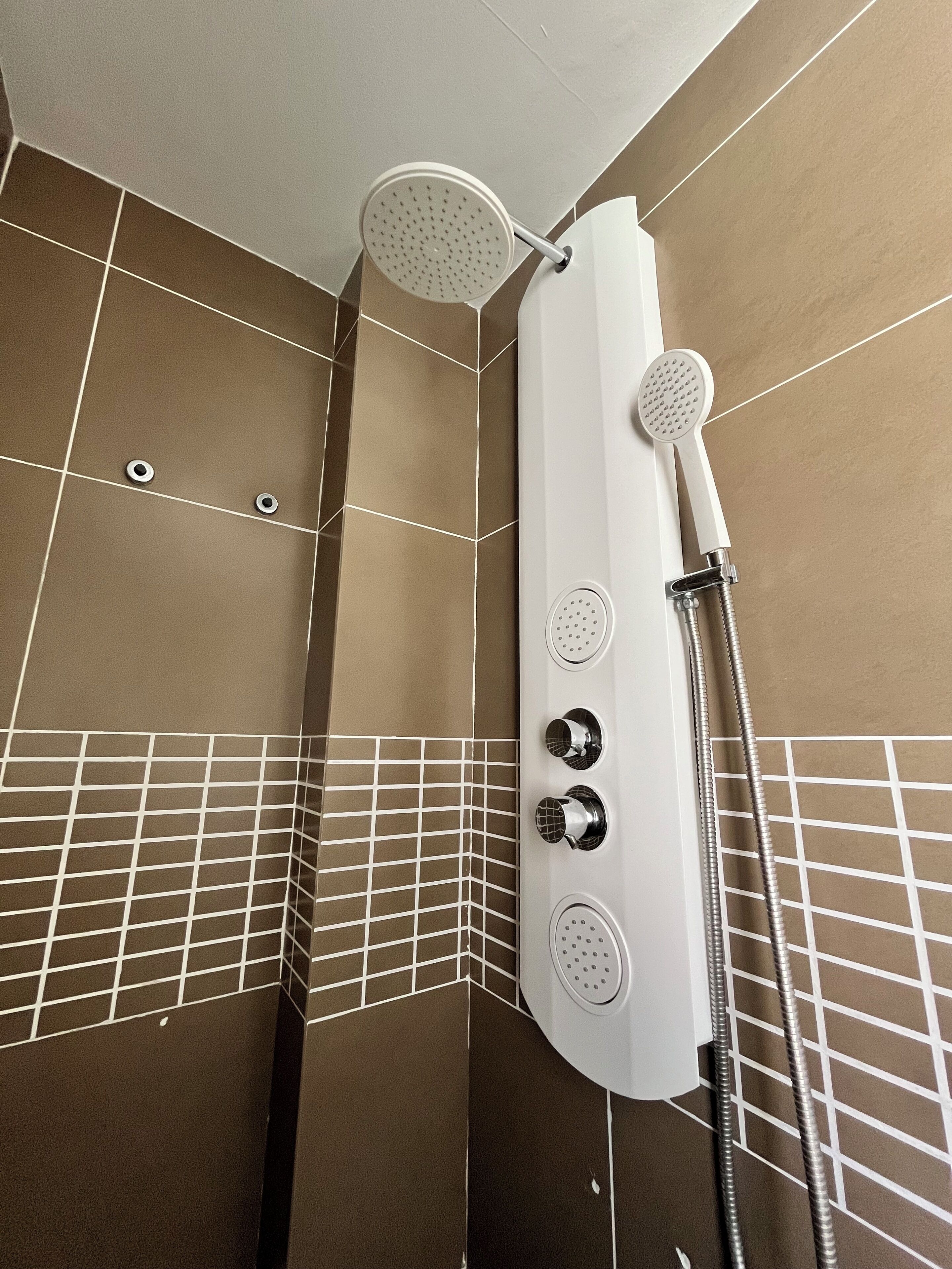A shower with multiple heads, a handheld showerhead, and a handheld shower hose.