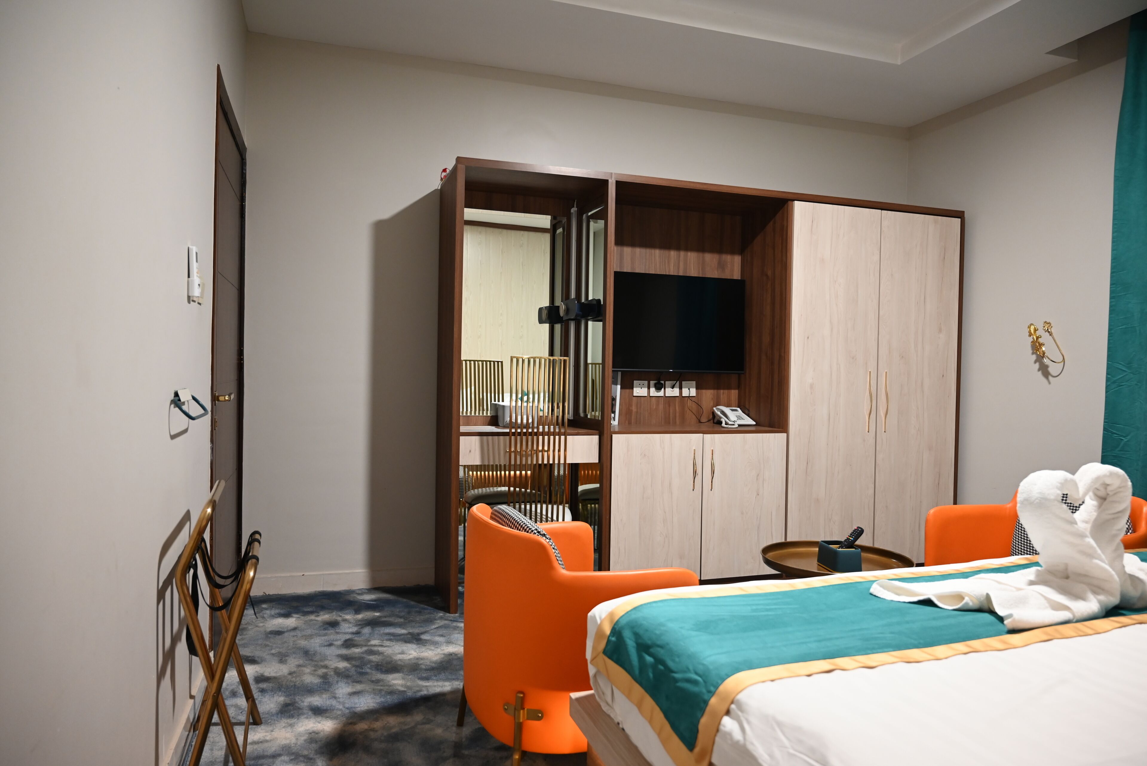 Ein Hotelzimmer mit einem Bett, orangefarbenen Sesseln, einem Schreibtisch, einem Fernseher und einem Kleiderschrank.