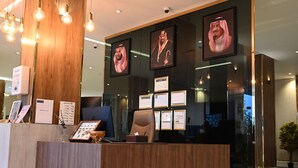 A reception desk with framed portraits, a wooden reception area, and a glass wall displaying certificates. - Relax Palace Hotel (Abha)