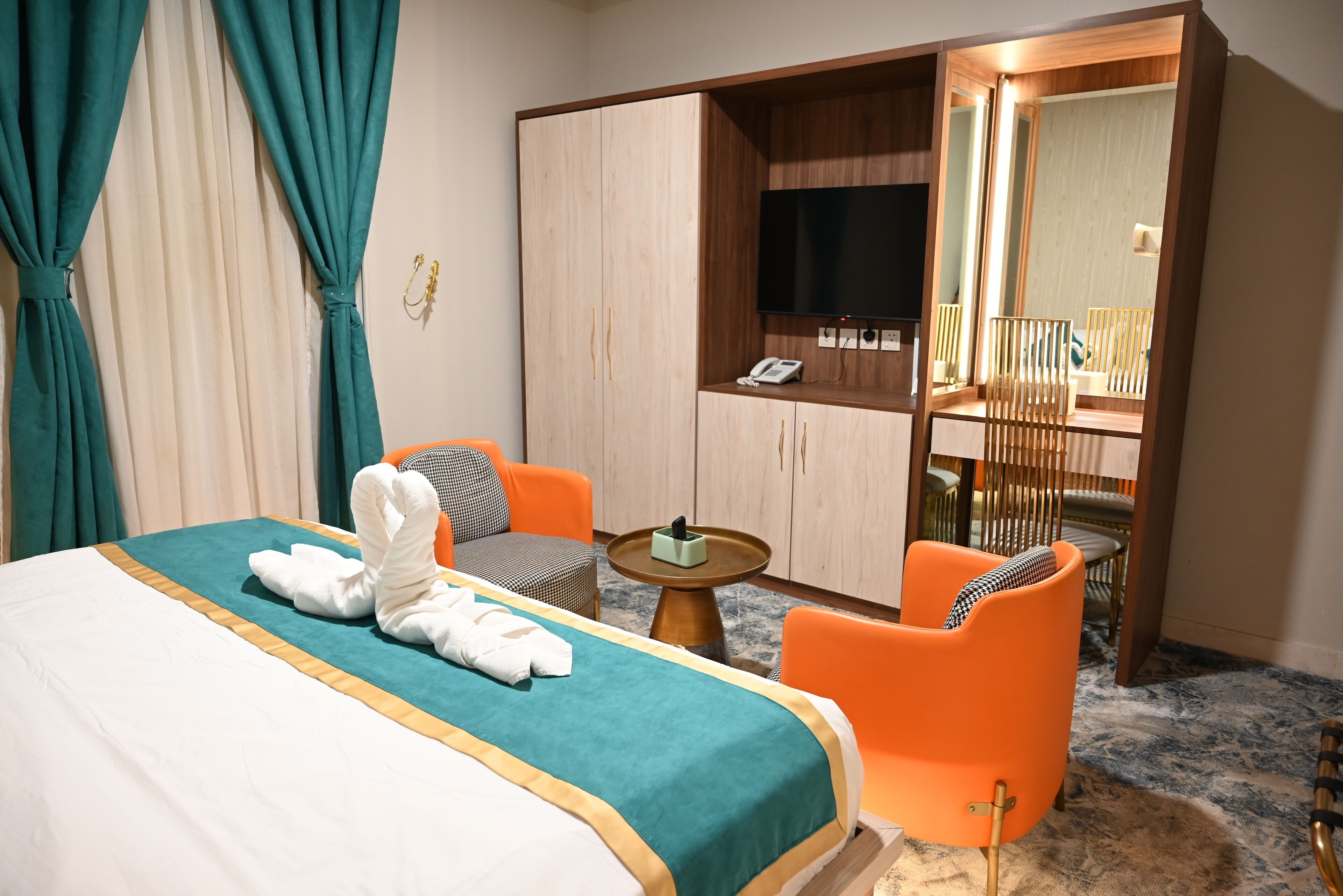A hotel room with a bed, two chairs, a small table, a wardrobe, a mirror, and a TV.
