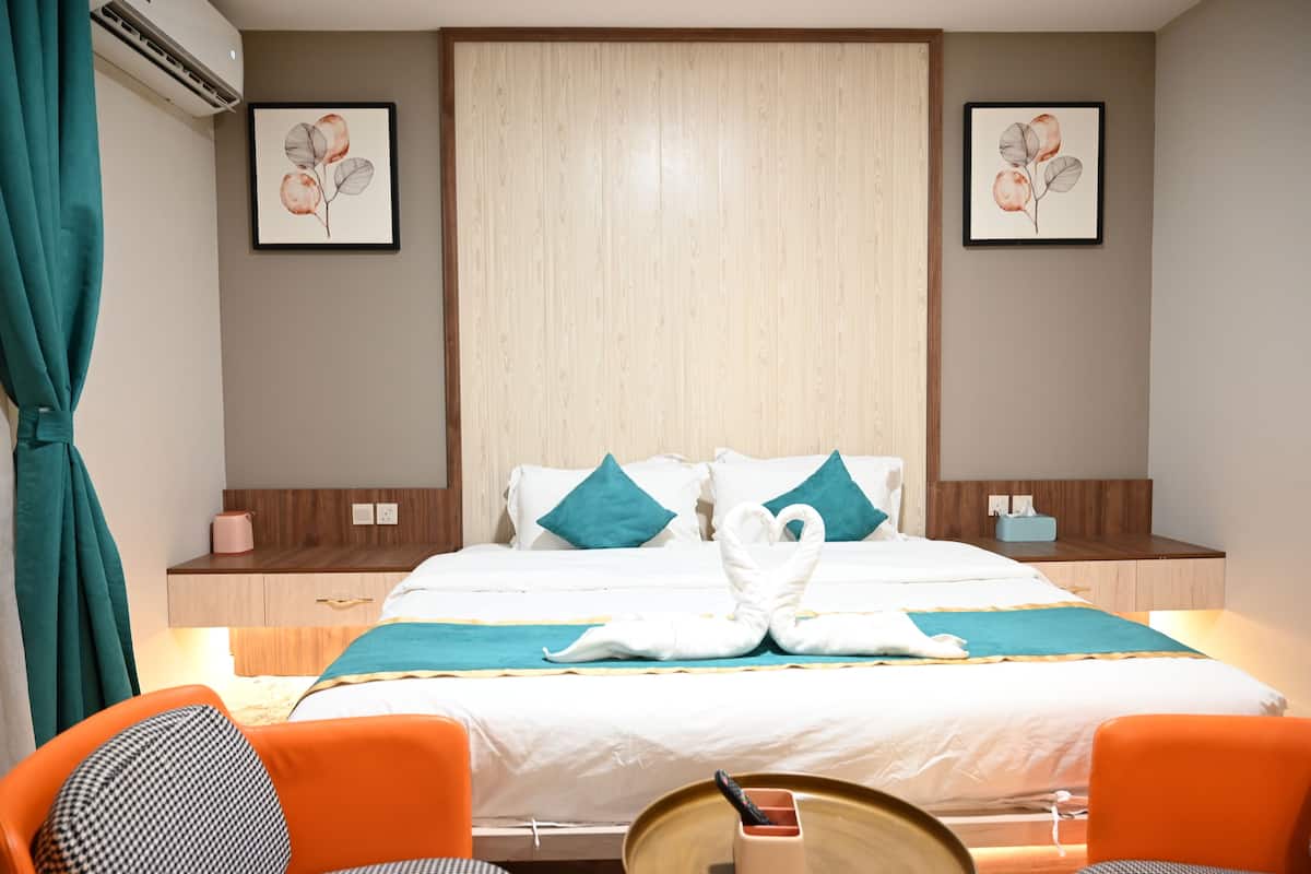 A hotel room with a bed, two pillows, a bedside table, a chair, and a wall-mounted air conditioner.