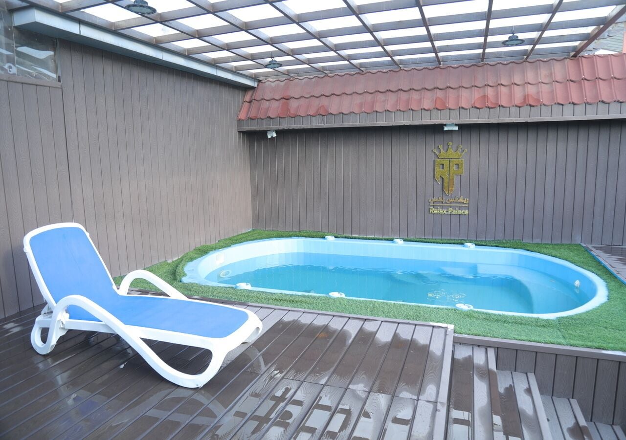 A swimming pool with a lounge chair, surrounded by wooden decking and a covered area with a red roof.
