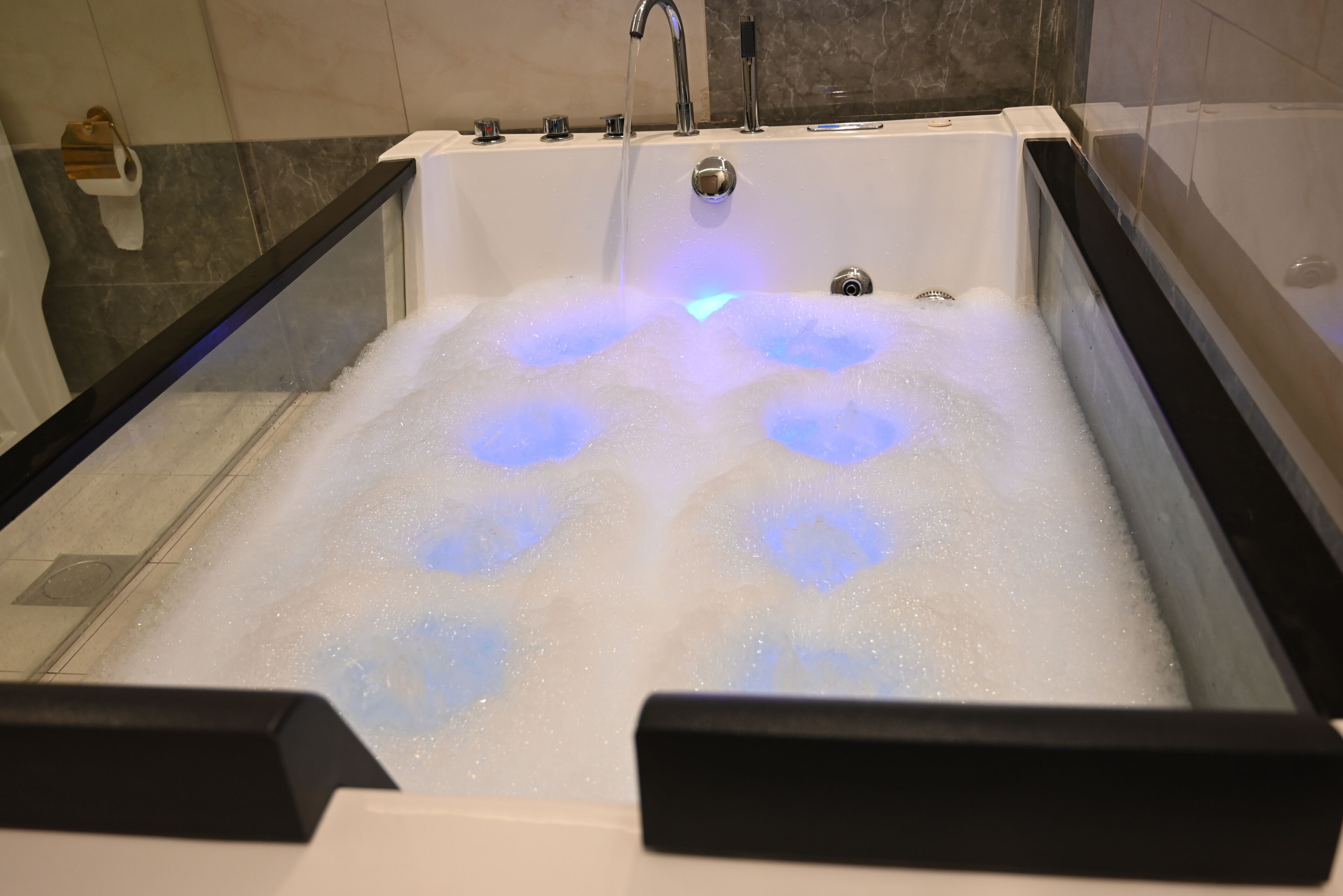 A bathtub with multiple jets of water, a visible drain, and a soap dispenser on the wall.