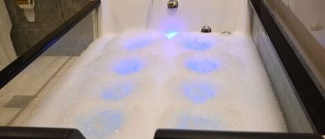 A bathtub with multiple jets of water, a visible drain, and a soap dispenser on the wall.