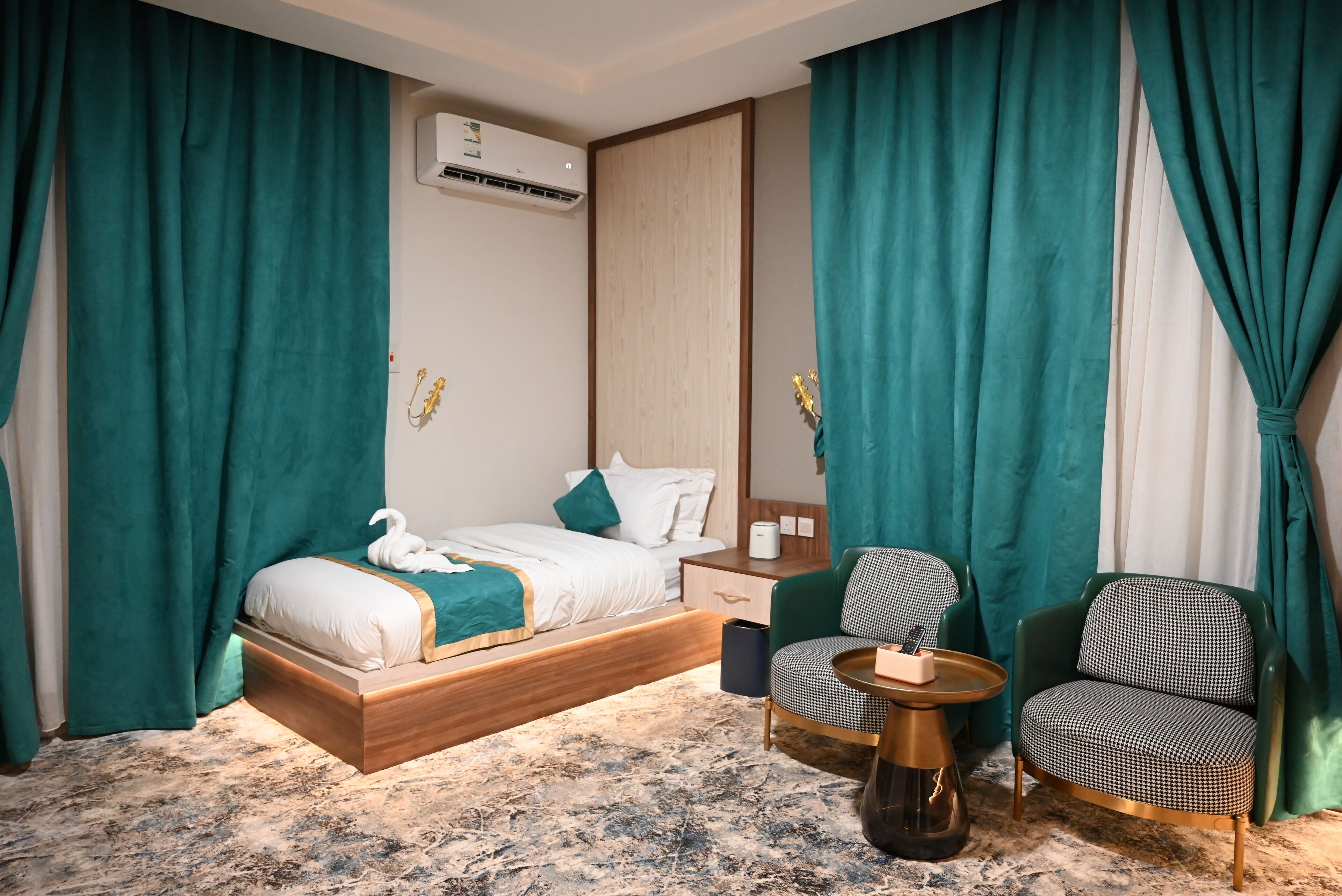A hotel room with a bed, two chairs, a small table, and an air conditioning unit.