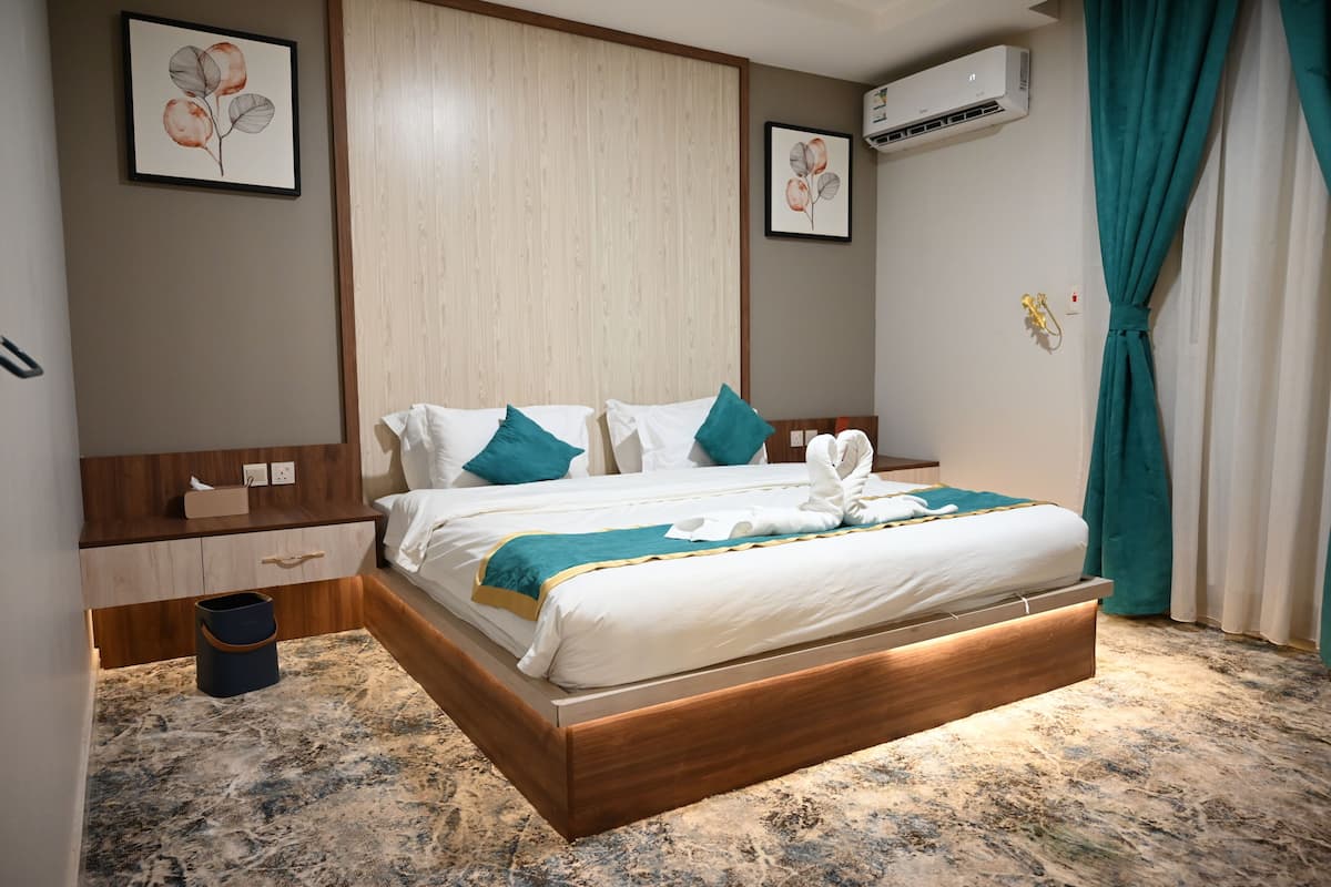 A neatly made bed with white and teal bedding, a wooden headboard, and a small bedside table with a lamp.