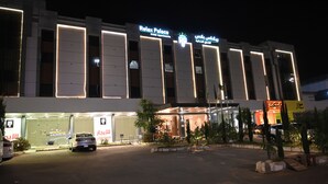 A modern hotel with illuminated signage, a parking lot, and a landscaped entrance area. - Relax Palace Hotel (Abha)