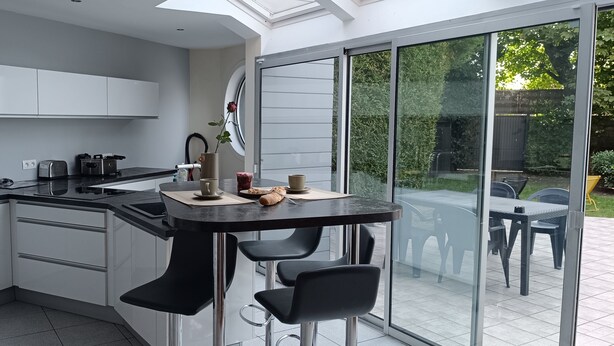 Cocina moderna con armarios blancos, encimera negra y comedor con mesa y sillas de vidrio.
