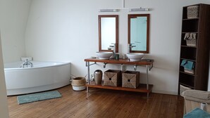 Un baño moderno con una bañera independiente, un tocador con un espejo grande y un estante de madera con cestas.