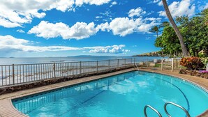 En pool med utsikt över havet, omgiven av ett trädäck och ett staket av metall.