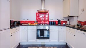 A kitchen with white cabinets, a red-tiled backsplash, a stainless steel range hood, and a black oven.