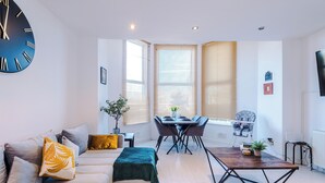 A modern living room with a sofa, coffee table, dining table, and a large wall clock.