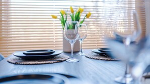 A dining table set with plates, cutlery, and glasses, with a vase of yellow flowers in the background.