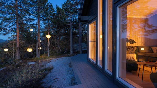 Una casa moderna con amplios ventanales, una terraza de madera e iluminación exterior.