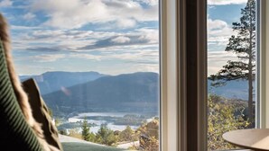 A room with a large window offering a view of mountains and a lake. - Wellness hut with panoramic view and home gym (Telemark)