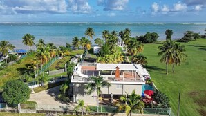 A two-story house with a balcony overlooking a beach, surrounded by palm trees and a clear view of the ocean. - New listing! Spacious 4-bedroom, water-front house in Las Picuas, Río Grande. (Río Grande)