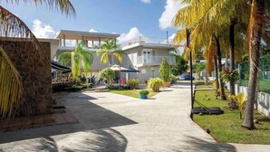 A residential area with a paved walkway, palm trees, and a two-story building with balconies. - New listing! Spacious 4-bedroom, water-front house in Las Picuas, Río Grande. (Río Grande)