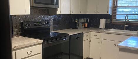 A kitchen with white cabinets, a black stove, a microwave, and a window with blinds.