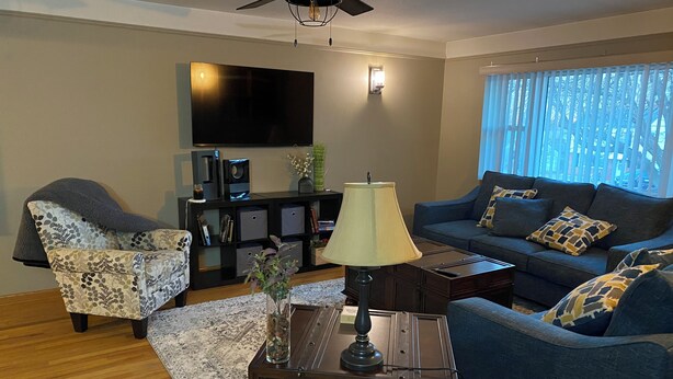 A living room with a sofa, armchair, and a coffee table. There is a TV mounted on the wall and a ceiling fan. - Spacious Beautiful Omaha Retreat - 2BR/1BA Apartment with All-Inclusive (Omaha)