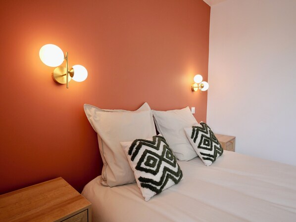 A neatly made bed with two pillows, a wooden nightstand, and two wall-mounted light fixtures.