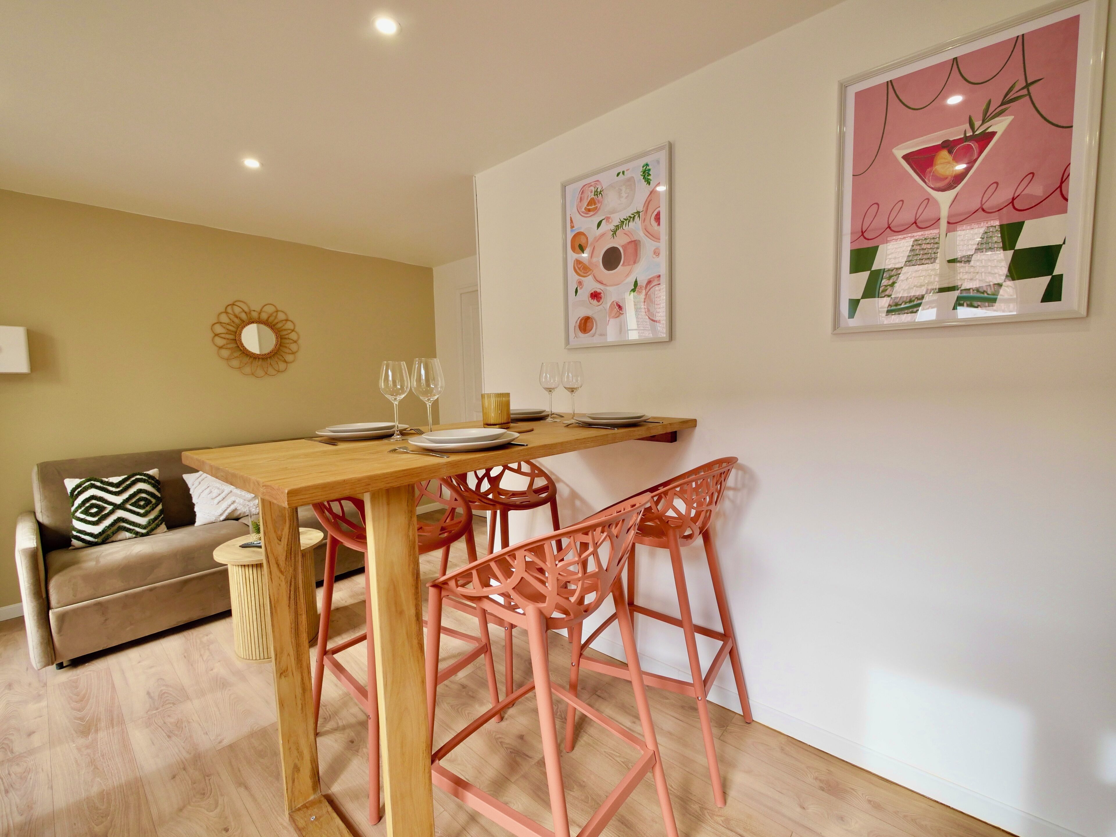 A dining area with a wooden table, pink chairs, and two framed pictures on the wall.