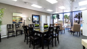 A conference room with a glass table, black chairs, a painting, and a view of palm trees. - Beachfront 2-bedroom condo with Gym, Pool, & WiFi, on  Jacksonville Beach. (Jacksonville Beach)
