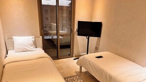 Une chambre d’hôtel avec deux lits, une télévision, une petite table ornée d’un vase de fleurs et une vue sur l’extérieur grâce à une porte coulissante.