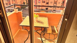 Un balcon avec une table et des chaises, un pot de fleurs et une vue sur un quartier résidentiel.