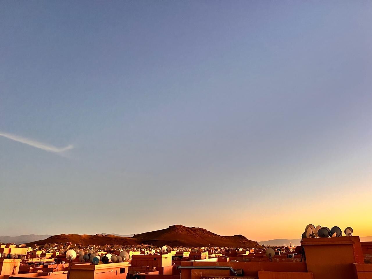 A cityscape with a prominent hill in the background and multiple satellite dishes on rooftops.