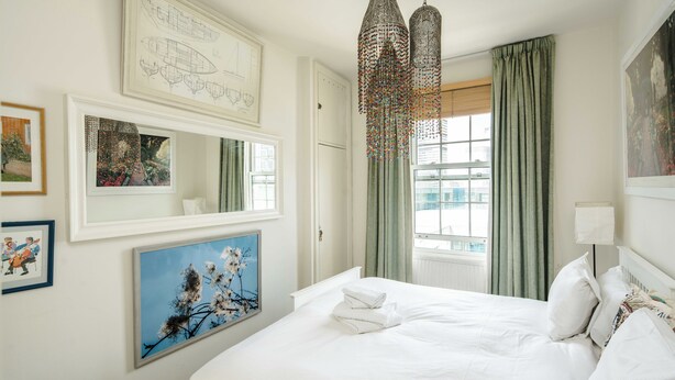 A neatly arranged bedroom with a large bed, a mirror, and artwork on the walls.