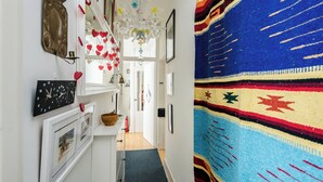 A hallway with a patterned rug, a clock, framed pictures, and a chandelier.