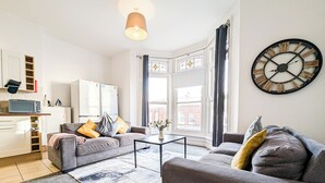Een moderne woonkamer met een grijze bank, een salontafel en een grote wandklok.
