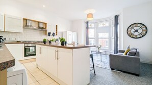 Een moderne keuken met witte kasten, een centraal eiland en een zithoek met een grijze bank.