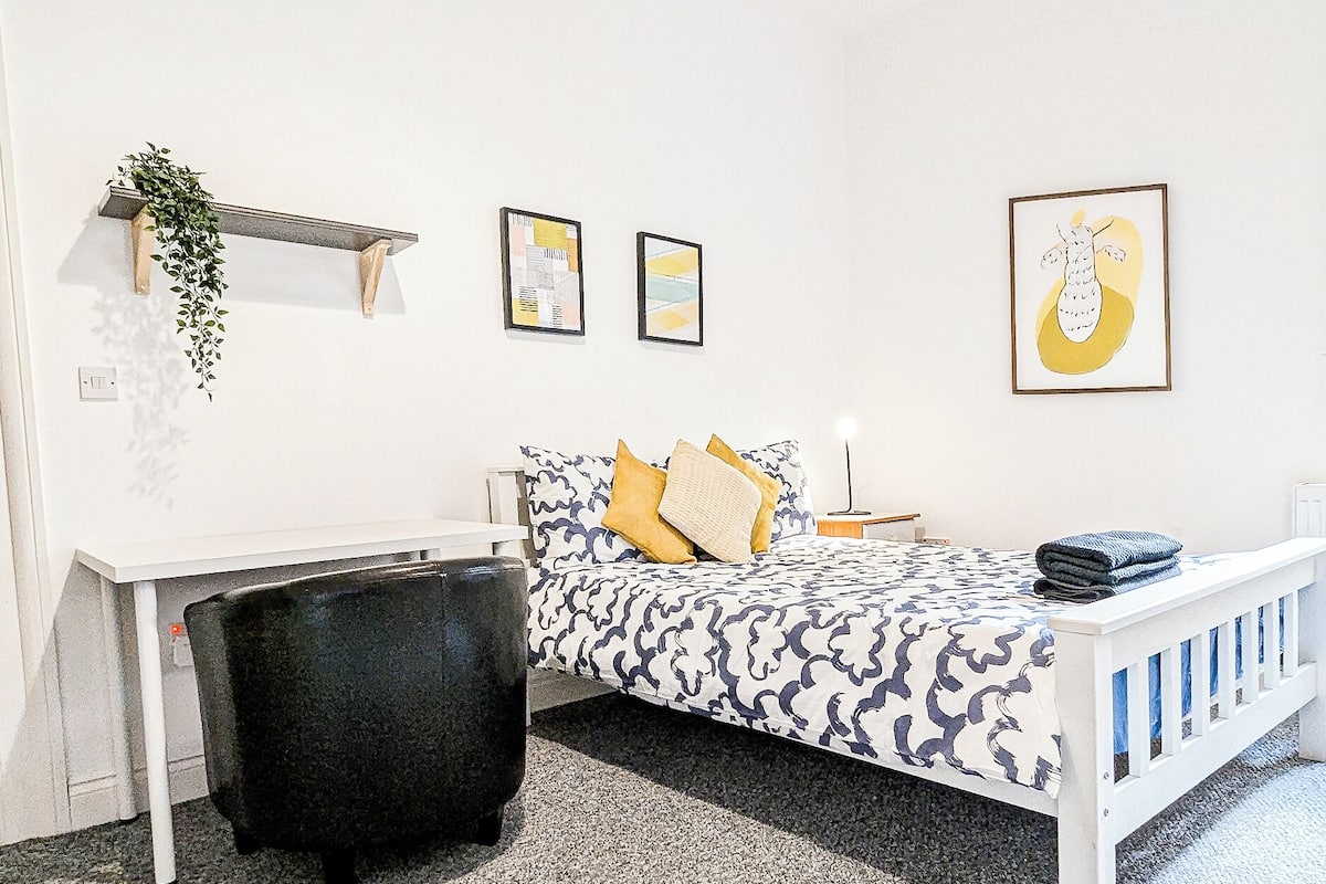 Un dormitorio con cama, escritorio, silla y una planta.