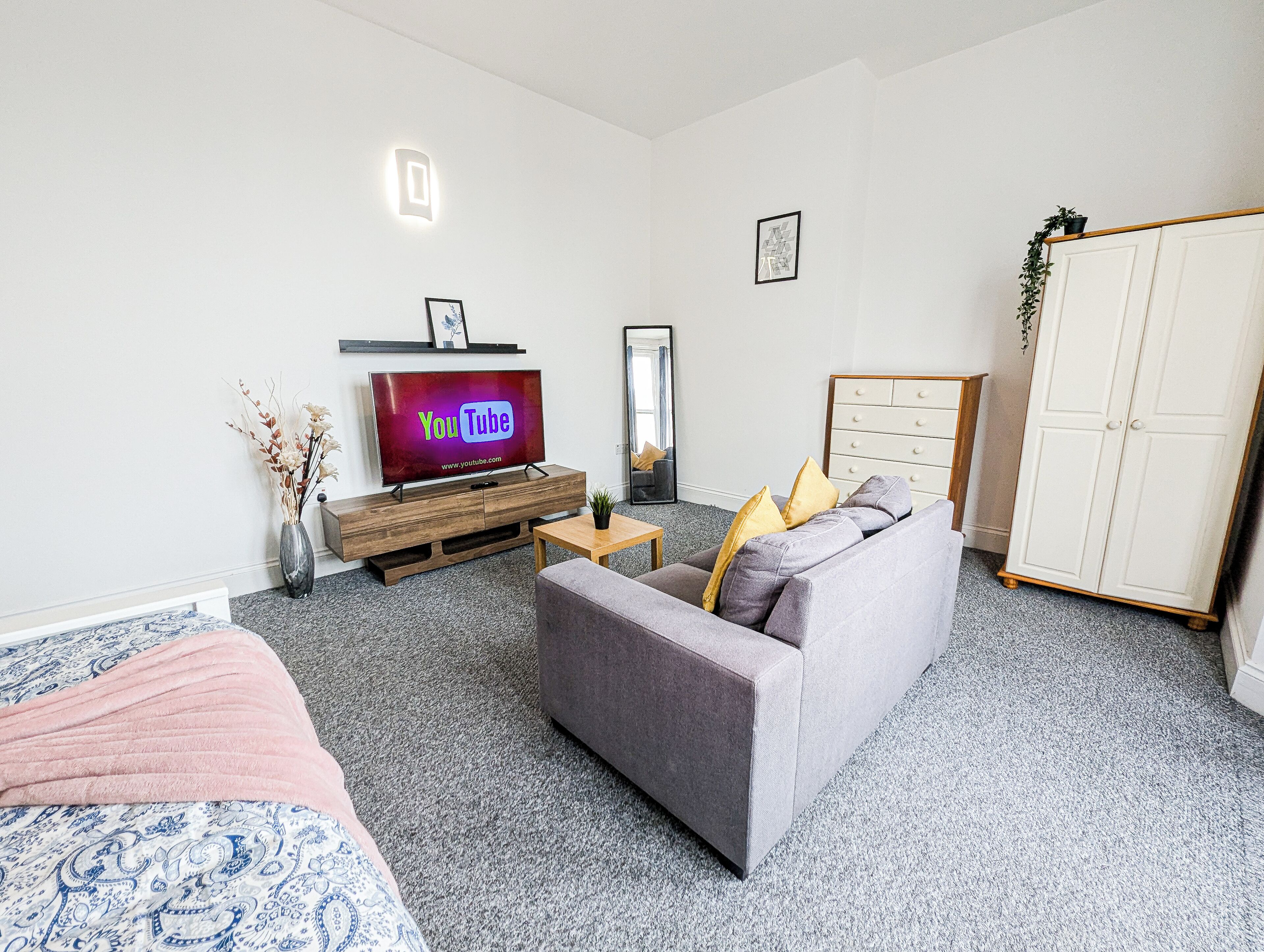 A modern living room with a grey sofa, a wooden TV stand, a small table, and a white wardrobe.