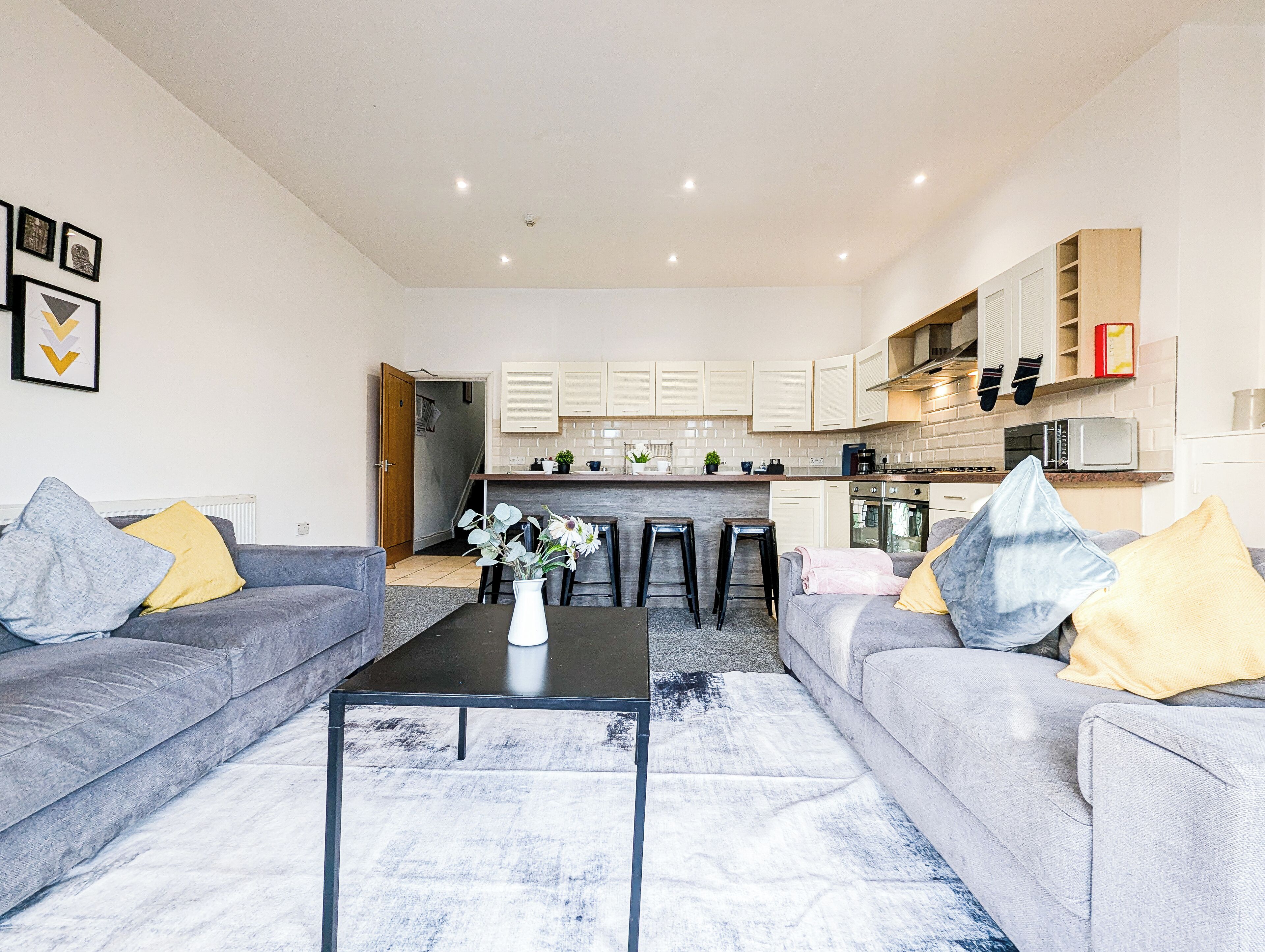 A modern living room with grey sofas, a coffee table, and a kitchen in the background.