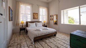 Un dormitorio con una cama de madera, dos mesitas de noche con lámparas, un aparador verde y una ventana con cortinas.