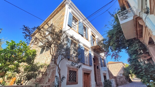 Un edificio tradicional de dos pisos con fachada de piedra, puerta de madera y balcón con barandilla de metal.