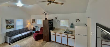 A compact living space with a sofa, a dining table, a kitchen area, and a ceiling fan.
