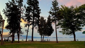 A park with picnic tables and benches, surrounded by tall trees and a view of the water. - Keep it simple at this peaceful and centrally-located place.  (Polson)