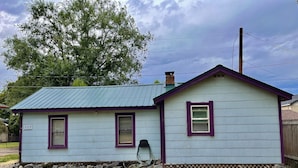 A small, single-story house with a number 707 sign, a metal roof, and a wooden fence in the background. - Keep it simple at this peaceful and centrally-located place.  (Polson)