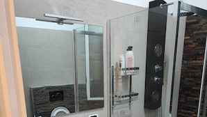 A modern bathroom with a white sink, wooden vanity, a large mirror, a glass shower enclosure, and a built-in soap dispenser. - Stella Polare Sensorial Home (Rome)
