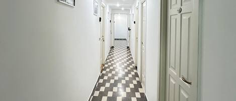 A hallway with a checkered floor, white walls, and doors on both sides.