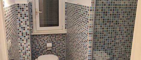 A bathroom with a toilet, sink, and shower area, featuring blue-tiled walls and a glass shower enclosure.