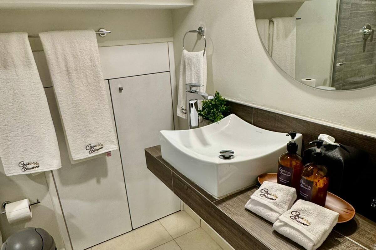Un baño moderno con un lavabo blanco, un espejo grande y una zona de ducha. Hay toallas y artículos de aseo en la encimera.