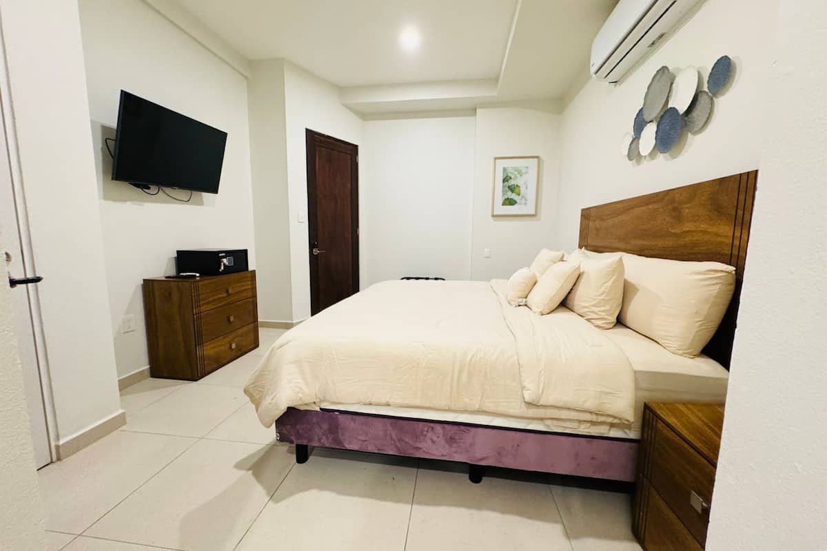 Un dormitorio con cama, cómoda, televisor y aire acondicionado.