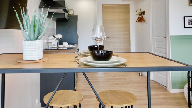 A modern kitchen with a wooden table, two stools, a potted aloe plant, and a wine glass.