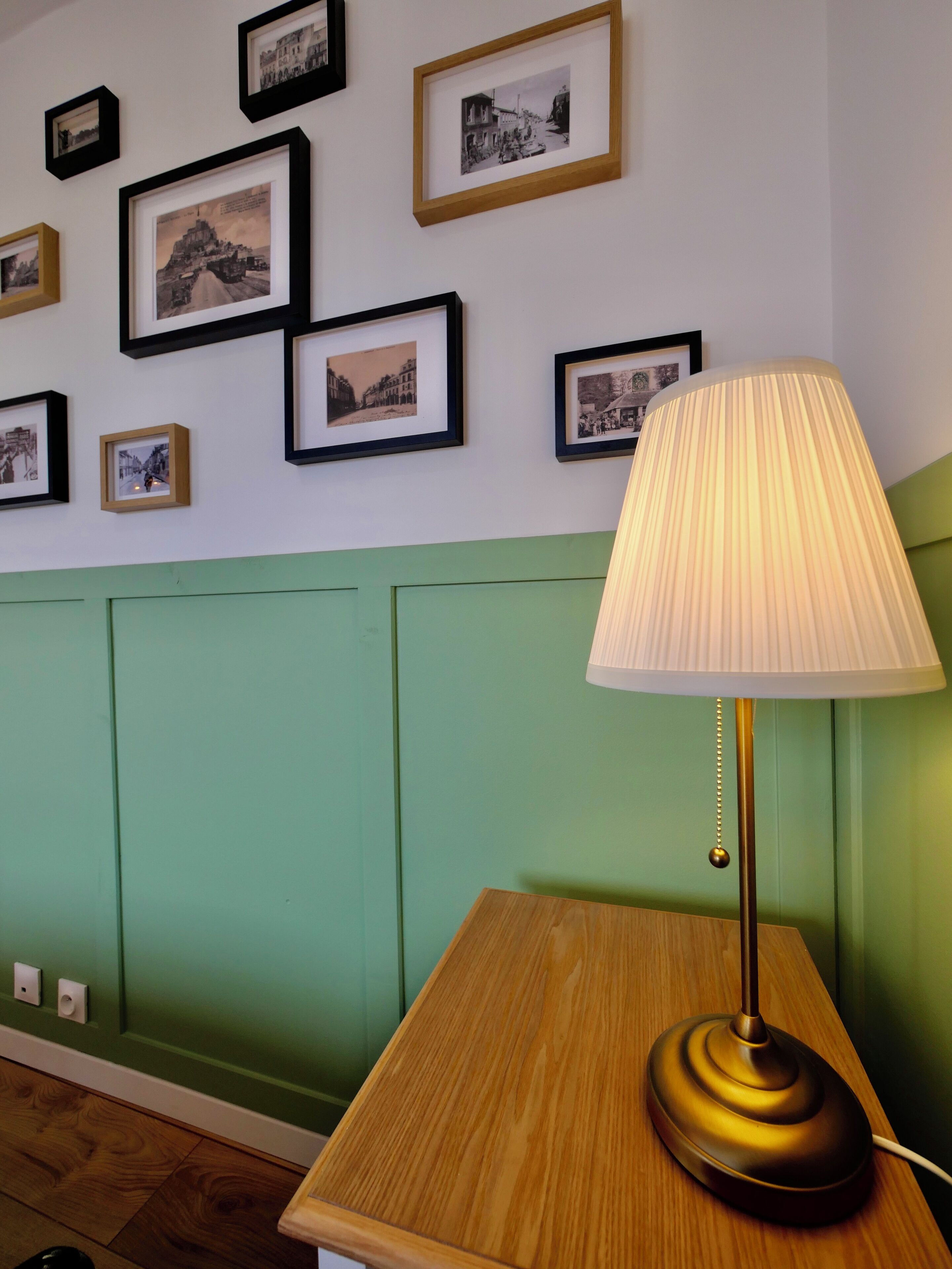 A room with a wooden table, a lamp, and a wall decorated with framed black and white photographs.