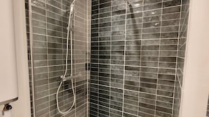 A glass-enclosed shower with a handheld showerhead and a fixed overhead showerhead.